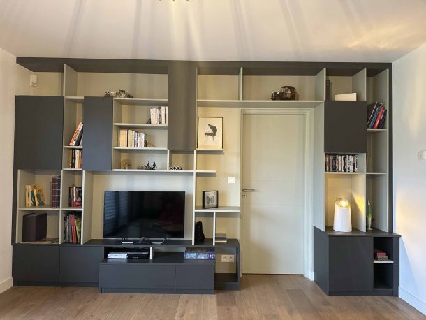 Bibliothèque murale sur mesure avec rangements ouverts et fermés, intégrant un espace pour la télévision, des étagères décoratives et des finitions en noir mat et beige, offrant une solution de rangement élégante et moderne.