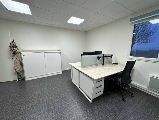 Bureau de collaborateurs aménagé avec un poste de travail sur mesure en bois clair et blanc, équipé de supports d'écrans doubles, un siège ergonomique, et un meuble de rangement à portes coulissantes dans un espace professionnel épuré.